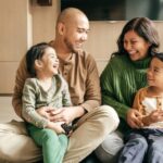 A family of four enjoys a joyful family day, sitting on the floor and laughing together in their cozy living room.