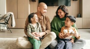 A family of four enjoys a joyful family day, sitting on the floor and laughing together in their cozy living room.